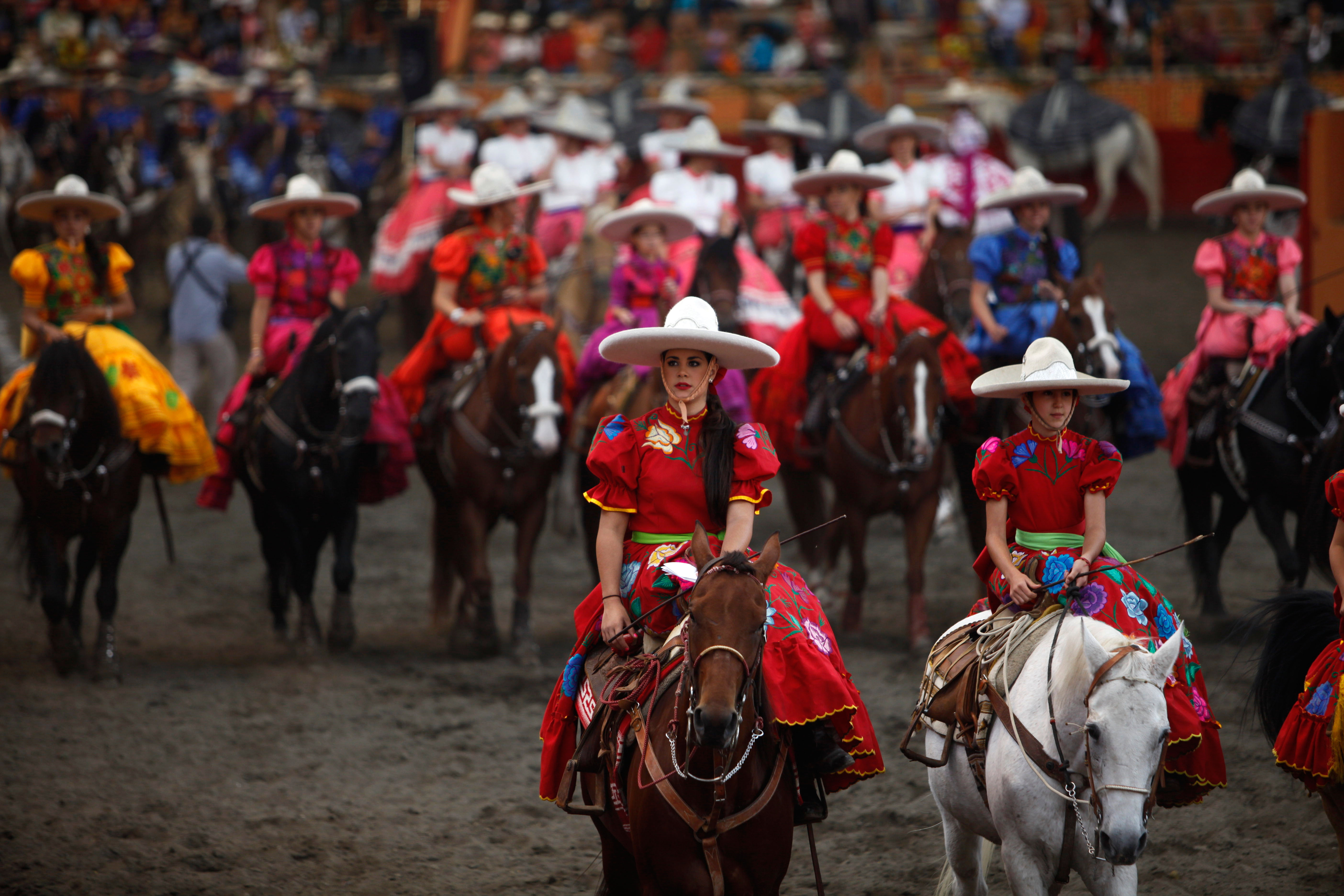 Women in colorful dresses and sombreros riding horses in a Mexican arena