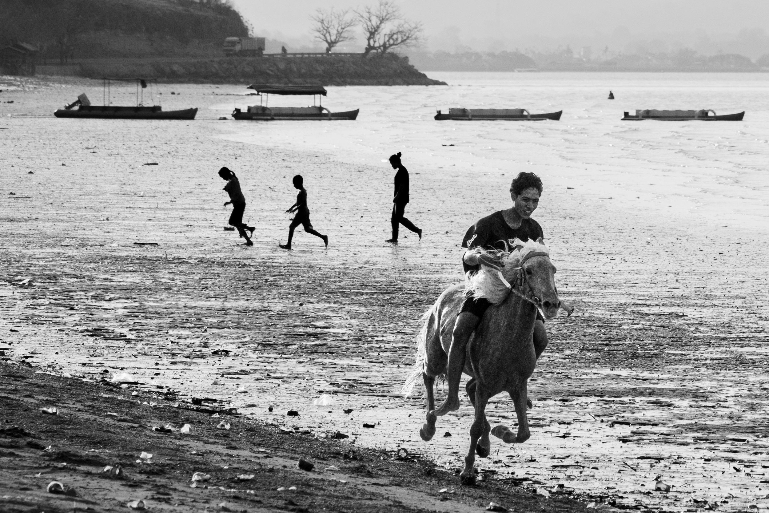 Boy riding a horse along a Sumba beach with children running alongside